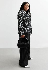 Zwart-witte geblokte blouse met lange mouwen, zwarte wijde broek en een kleine zwarte handtas. Inclusief zilveren puntige schoenen.