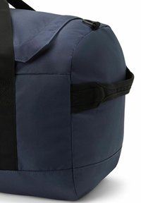 Marineblauwe stoffen sporttas met een ronde vorm, zwarte handvatten en een klep sluiting. Heeft een gladde textuur en versterkte stiksels op de naden.