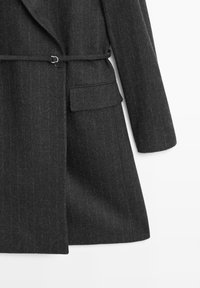 Mørkegrå uldfrakke med lodrette nålestriber, kløvet revers, bælteaccents og sidelomme, med en figursyet silhuet og glat tekstur.