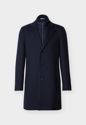 Manteau en laine bleu marine avec un col montant, une fermeture boutonnée simple, deux poches latérales et une doublure intérieure matelassée.