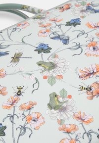 Tekstylia w kwiatowy wzór, z zielonymi żabami, owadami i różnymi kwiatami w pastelowych kolorach. Miękka tekstura na jasnoniebieskim tle.