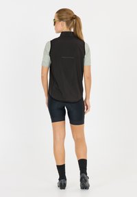 Schwarze ärmellose Weste über einem hellgrünen Kurzarmhemd, kombiniert mit navyblauen Radshorts. Reflexionselemente und tailliertes Design.