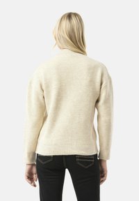 Romige, geribde trui met een relaxte pasvorm en verlaagde schouders. De trui heeft een ronde halslijn en eindigt op de taille, gecombineerd met donkere jeans.