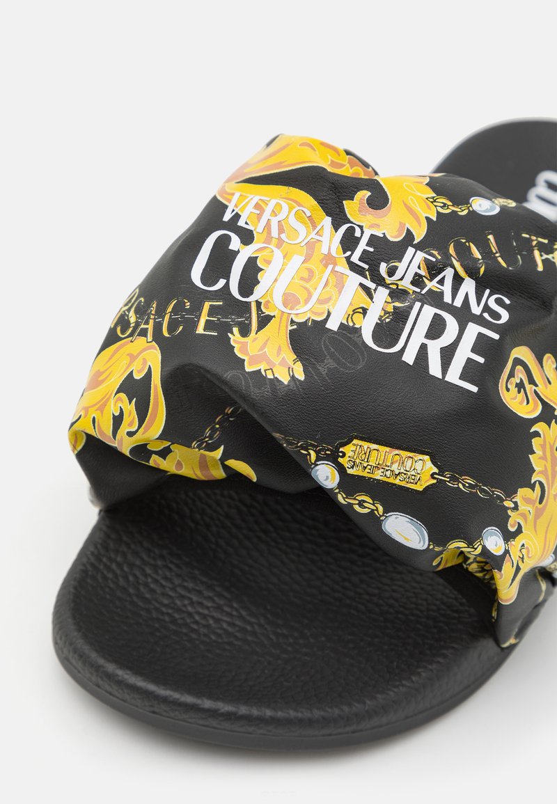 Czarna klapek z wzorzystym paskiem z złotymi i żółtymi barokowymi wzorami oraz białym tekstem "VERSACE JEANS COUTURE". Teksturowana wkładka.