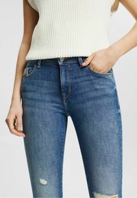 Mörkblå skinny jeans i denim, med slitna lappar, hög midja och en klassisk femficksdesign.