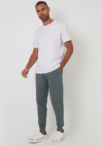 Weißes Baumwoll-T-Shirt kombiniert mit dunklen grünen Jogginghosen und weißen Sneakers. Lässiges Design mit Taschen und gerippten Bündchen an den Hosen.
