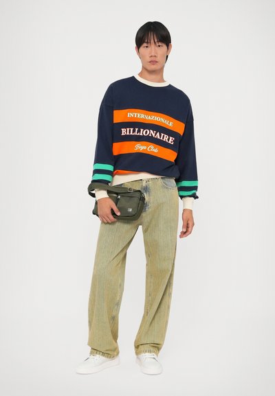 Sweatshirt azul-marinho com riscas laranja e verde, com a inscrição "Billionaire Boys Club". Calças largas verde-claro e uma bolsa cruzada verde-azeitona.