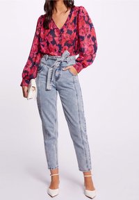 Blusa de manga larga con estampado floral en tonos rojos y marinos, combinada con unos vaqueros de cintura alta de mezclilla ligera y tacones blancos.