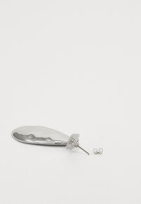 Zilveren studoorbel met een gebogen, langwerpige vorm en reflecterend oppervlak, vergezeld van een kleine oorbelsteun in een minimalistisch ontwerp.