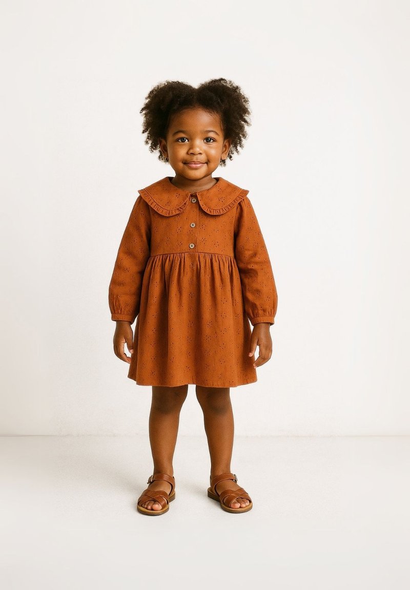 Šatové šaty v rezavé barvě s kulatým límcem, dlouhými rukávy, předními knoflíky a květinovým vzorem. Skombinováno s hnědými sandály na pásku.