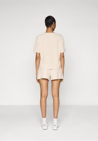 Ensemble lounge beige côtelé comprenant un haut à manches courtes et un short, conçu avec une coupe décontractée et une texture subtile, porté avec des baskets blanches.