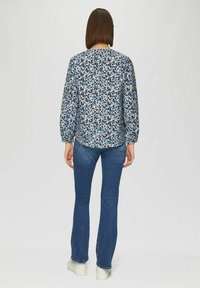 Marineblauwe blouse met geometrische patronen, lange mouwen en elastische manchetten, gecombineerd met flared jeans en witte sneakers.