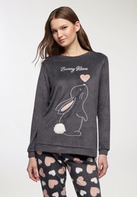 Felpa grigia in pile con una grafica di coniglio e un cuore, accompagnata dalla scritta 'Bunny Kisses'. Abbinata a pantaloni pigiama con stampa a cuori.