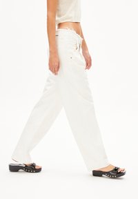 Wijdvallende witte broeken met een ruwe zoom, gecombineerd met zwarte platform sandalen met een glanzende afwerking en decoratieve hardware.