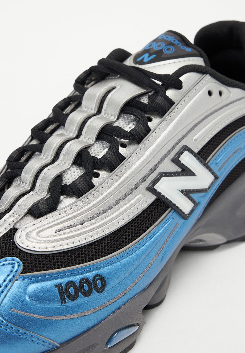 Graue und schwarze Sneaker mit blauen Akzenten, bestehend aus Mesh- und Lederstoffen, gepolsterter Sohle und auffälligen Logo-Details.