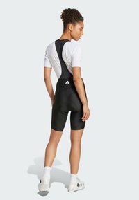 Schwarze Radsport-Bib-Shorts mit verstellbaren Trägern, ausgestattet mit einem gepolsterten Sitz, glatter Textur und kontrastierendem weißen Logo auf der Rückseite.