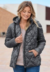 Grau gesteppte Jacke mit Kapuze, mit einem Reißverschluss vorne, seitlichen Taschen und einer glatten, glänzenden Textur. Getragen über einem hellen Oberteil.