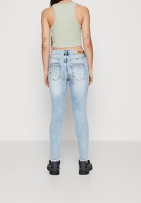 Jeans ajustados de color azul claro con un lavado descolorido y dos bolsillos traseros, combinados con una camiseta corta de color verde claro y calzado negro.