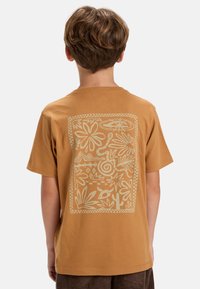 Camiseta de algodón marrón con un gran gráfico en colores claros, con diseños florales y abstractos en la parte posterior. Mangas cortas.
