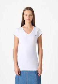 White cotton V-neck t-shirt with short sleeves, featuring a small black logo on the left chest side. Smooth texture and fitted design.