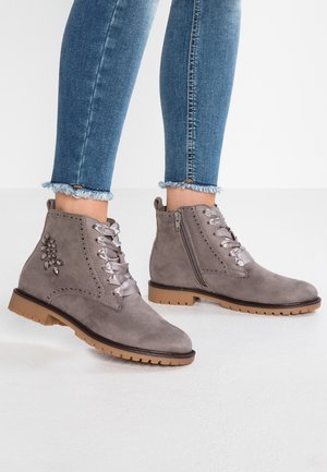 Des bottines en suédine grises présentent des coutures décoratives, des lacets en satin gris, une fermeture éclair et une semelle en caoutchouc marron avec une texture antidérapante.