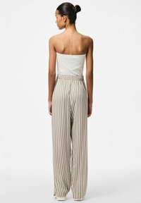 Strapless geribbelde top in het wit, gecombineerd met hoge taille, wijde broek met verticale beige en crèmekleurige strepen en een relaxed fit.
