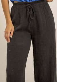 Pantalons larges noirs, texturés, avec une taille à cordon de serrage. Confectionnés en tissu léger, avec un motif de plis subtil.