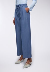 Pantaloni a gamba larga blu chiaro con una finitura testurizzata, cintura in vita e tasche laterali. Abbinati a décolleté slingback a punta grigia chiara.