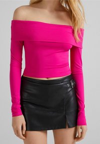 Tajtat off-shoulder topp i klarröd tyg med långa ärmar, kombinerad med en svart läder minikjol med en sidoknäppningsdetalj.