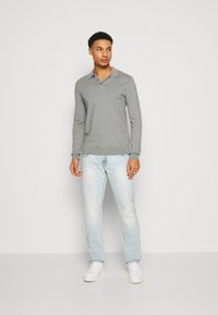 Gray long-sleeve polo shirt with a collar, paired with light blue jeans and white sneakers, standing against a plain background.