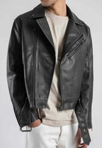 Giacca da biker in finta pelle nera con zip diagonale, colletto a scatto e polsini con cintura. Presenta una vestibilità slim e una finitura testurizzata.