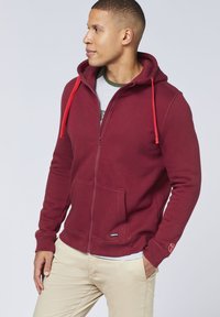 Bordeauxfarbener Reißverschluss-Hoodie mit roten Kordeln, Kängurutasche und Logodetail am Bündchen. Hergestellt aus weichem, strukturiertem Material.