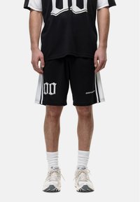 Zwart mesh basketbal jersey en shorts set met witte accenten, voorzien van grote cijfers en zijstrepen. Draag het met lichtgekleurde sneakers.
