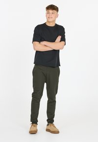 Zwarte korte mouwen t-shirt gecombineerd met olijfgroene tapered broek en tan schoenen. Eenvoudig ontwerp, zachte textuur en ruime pasvorm.