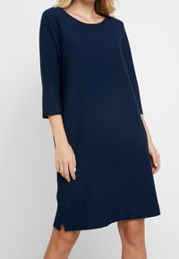 Granatowa sukienka z krótkim rękawem wykonana z teksturowanej tkaniny, z okrągłym dekoltem i rozcięciami po bokach u dołu, zapewniająca luźne, swobodne dopasowanie.