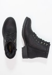 Černé kotníkové boty s texturovaným povrchem z umělé kůže, šněrováním vpředu, bočním zipem a silnou gumovou podrážkou. Podšívka uvnitř zajišťuje pohodlí.