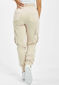 Pantaloni de trening cargo bej cu talie elastică, două buzunare spate și buzunare laterale cargo. Textură netedă, manșete ajustate la glezne.