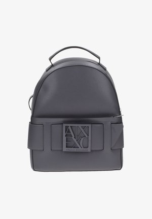 Sac à dos en cuir gris avec un haut arrondi, une base plate, des bretelles réglables et un grand patch logo à l'avant, avec une texture lisse.