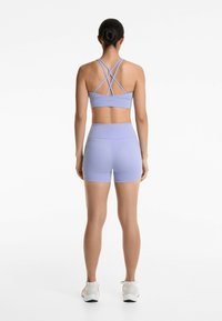 Sutien sport de culoare mov deschis, cu bretele în cruce, asociat cu pantaloni scurți ajustați de aceeași culoare. Materialul pare elastic și neted.