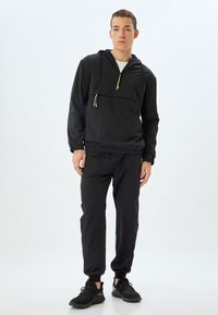 Svart lättviktsanorak med justerbar huva, halvdragkedja fram och elastiska ärmar. Matchas med avsmalnande byxor och svarta sneakers.