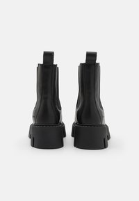 Sorte skinnankler med en slank design, som har elastiske sidestykker, pull-tabs og tykke, teksturerte gummisåler.