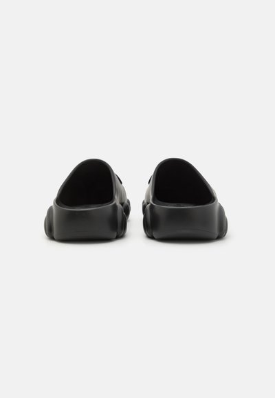 Zapatos de goma negros tipo zueco con punta redonda y suela acolchada. El interior tiene un acabado suave; el exterior es mate sin patrones visibles.