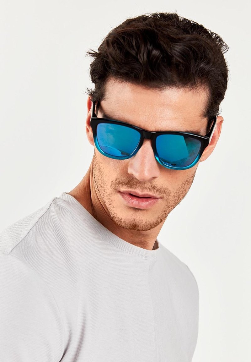 Ochelari de soare negri cu lentile reflective albastre, având un design elegant. Modelul poartă o cămașă scurtă, cu mânecă scurtă, texturată, de culoare gri deschis.
