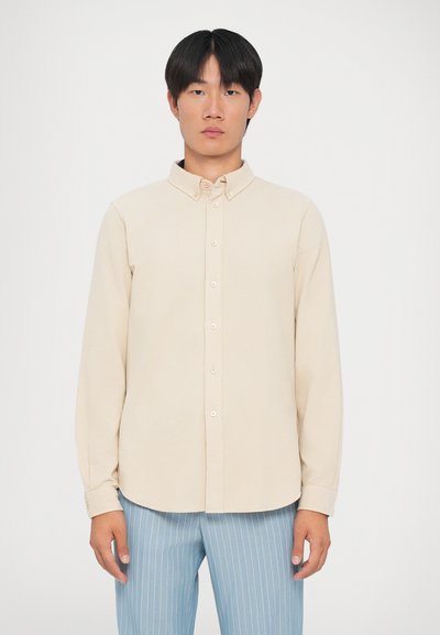 Beige button-up shirt with a spread collar, long sleeves, and a curved hem. Texture appears smooth, with light stitching details.