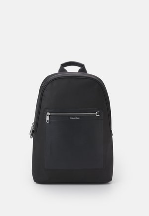 Sac à dos noir en nylon, doté d'une grande poche zippée à l'avant, d'un logo, d'un dessus arrondi et de bretelles doubles. Texture lisse.