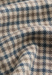 Vävt tyg som visar en houndstooth-mönster i beige, bruna och blå nyanser, med en texturerad yta och mjuk häng.