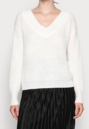 Maglione bianco lavorato a maglia con scollo a V profondo, texture a coste e maniche lunghe, abbinato a una gonna nera plissettata.