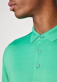 Πράσινο πόλο μπλουζάκι με κλασικό γιακά και δύο κουμπιά. Λείος υφασμάτινος χαρακτήρας με εφαρμοστή σχεδίαση, που τονίζει τις καθαρές γραμμές και την απλότητα.