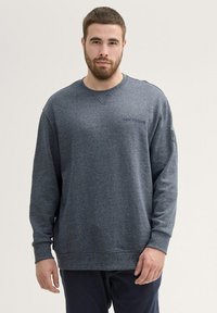 Donkerblauwe sweatshirt met lange mouwen, ronde hals en textuurstof. Heeft een klein logo op de borst en ribgebreide manchetten.