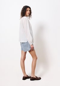 Weiß gestreifte Bluse mit langen Ärmeln, hellblaue Jeansshorts und braune Slipper. Die Bluse hat zarte vertikale Streifen und einen lockeren Schnitt.